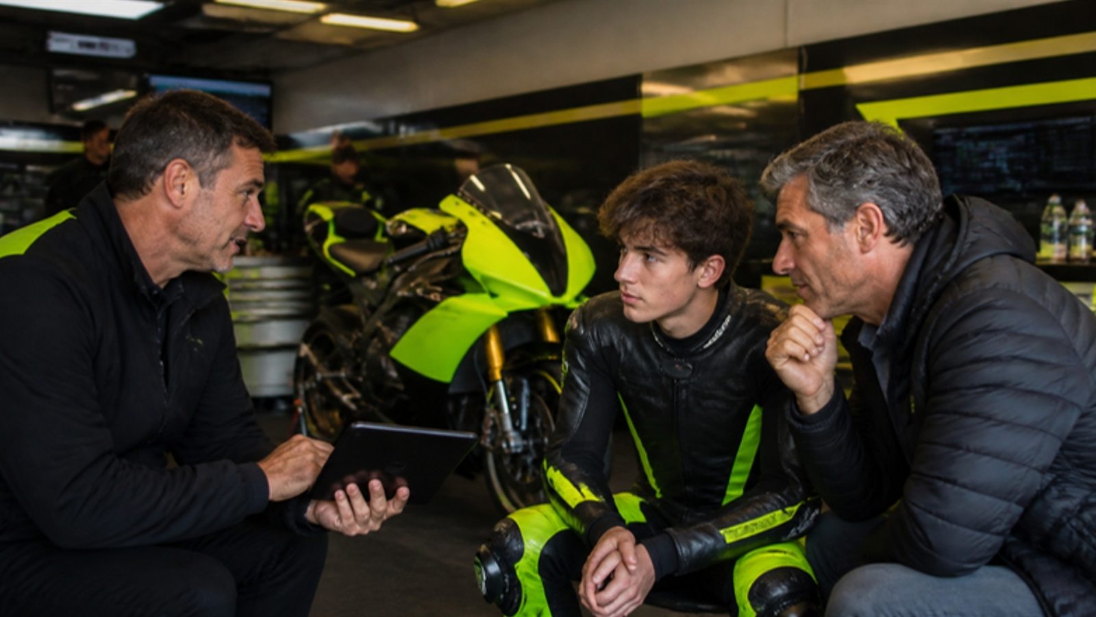 Il team principal parla con un giovane pilota e suo padre nel box