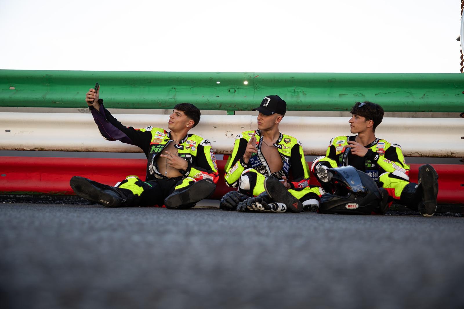 Tre piloti del team seduti a bordo pista con le tute nere e lime